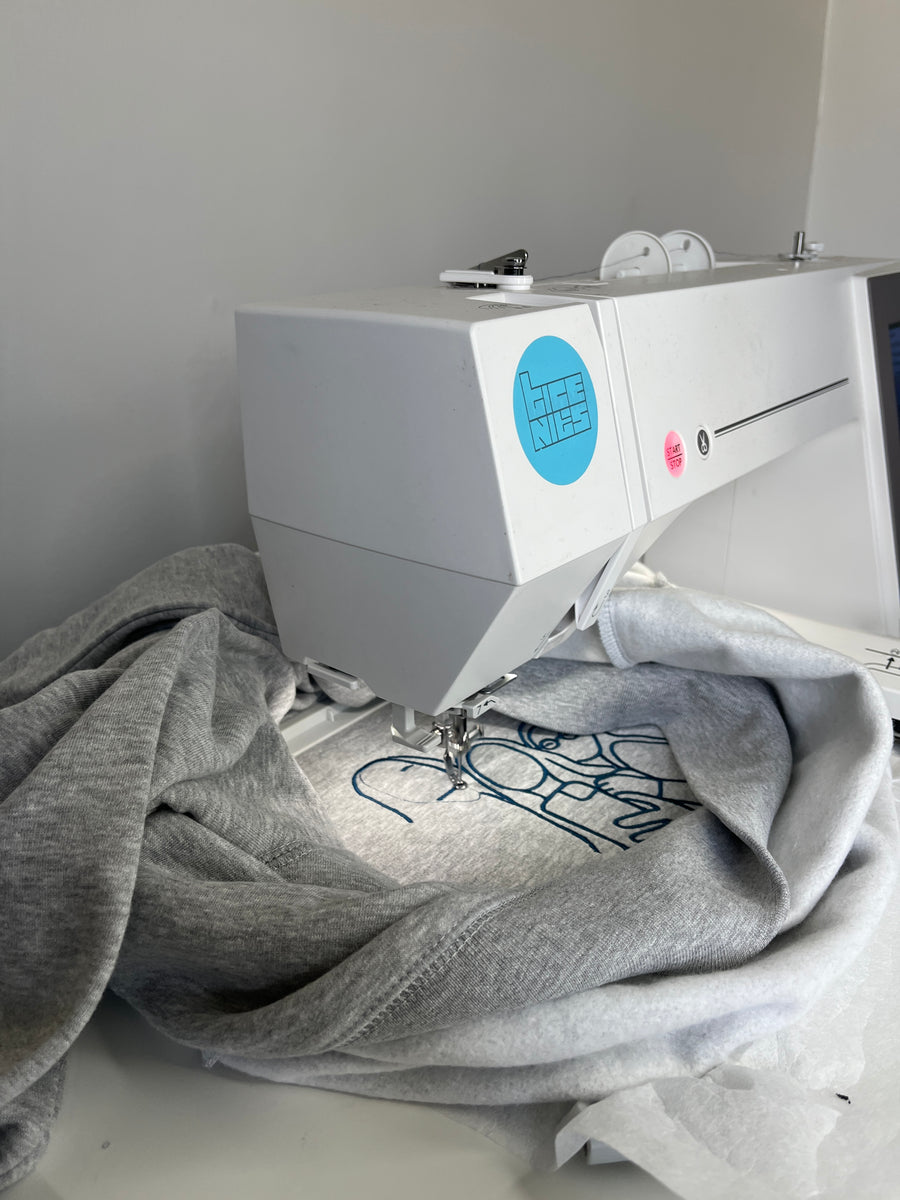 Notre première petite machine à broder à l'œuvre sur un sweat à capuche gris