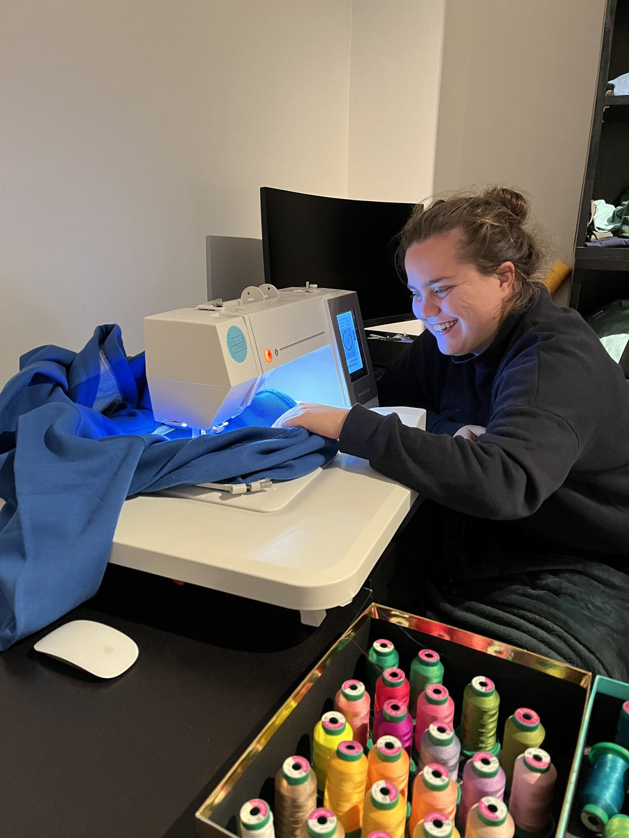 Julie riant devant la machine à broder, parmi les bobines de fil
