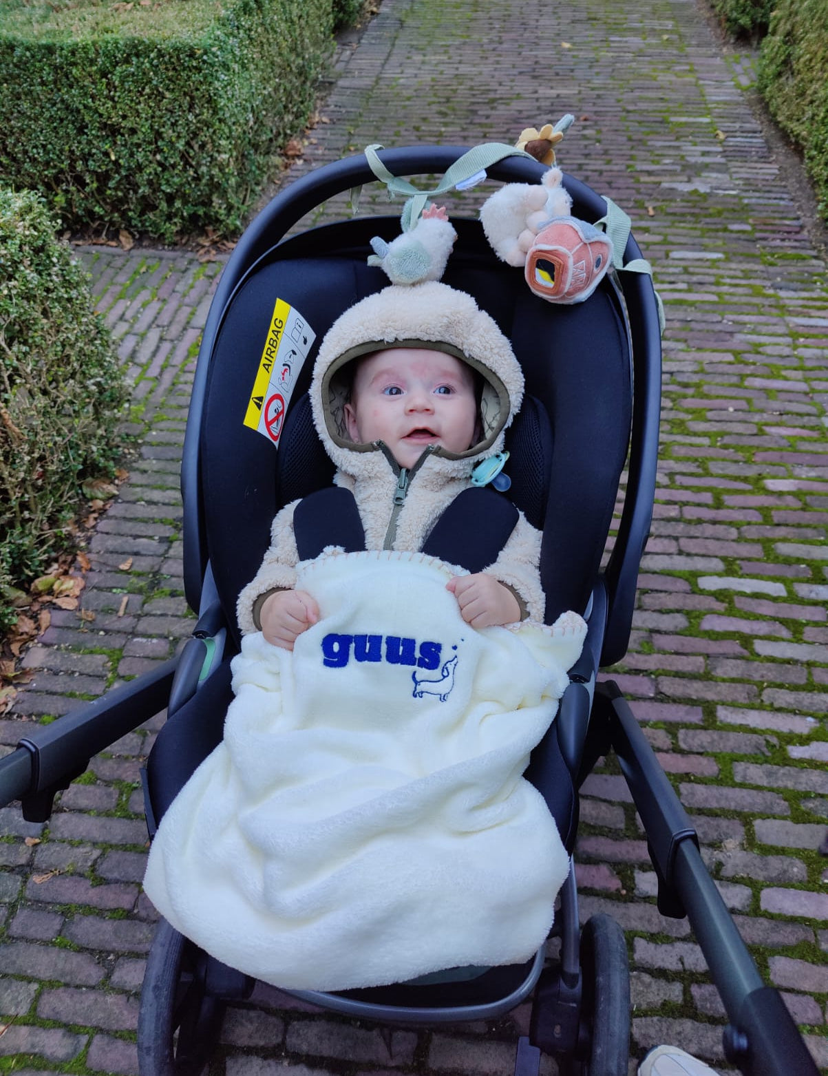 Baby in de kinderwagen onder een wit dekentje met geborduurde naam en hondje, geborduurd door Tice Nits