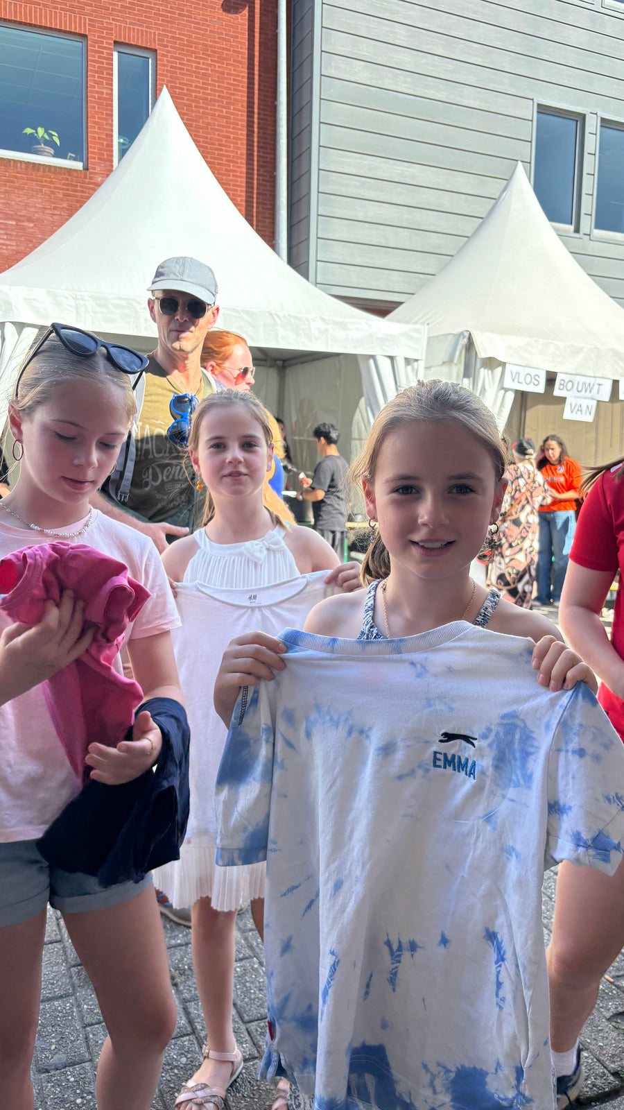 Des filles montrent un t-shirt tie-dye avec un nom brodé près de la tente
