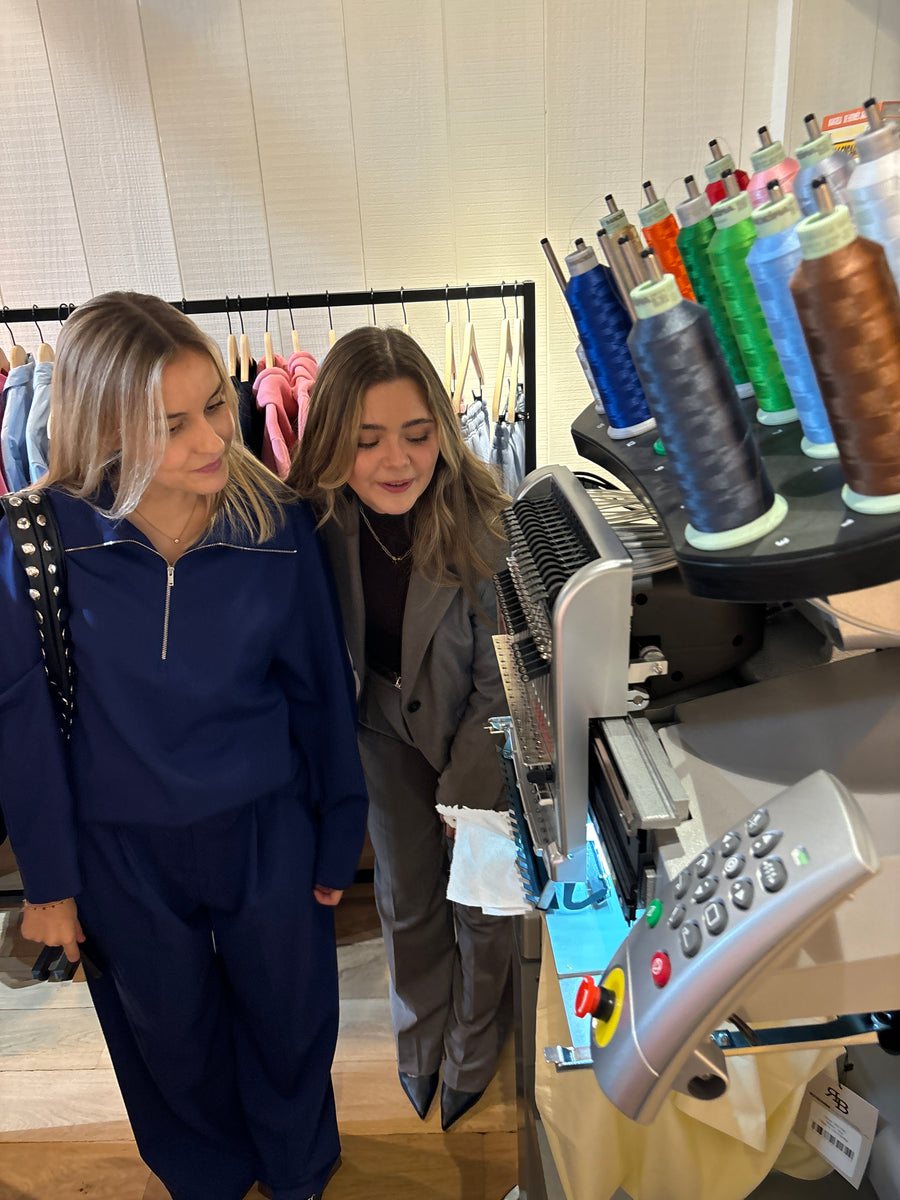 Deux femmes devant la machine à broder lors d'un pop-up dans un magasin de vêtements