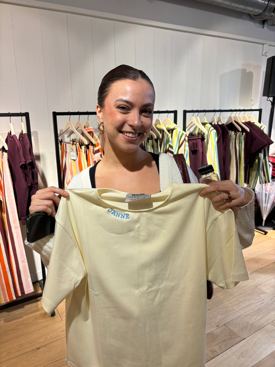 Une cliente montre son t-shirt crème brodé dans une boutique