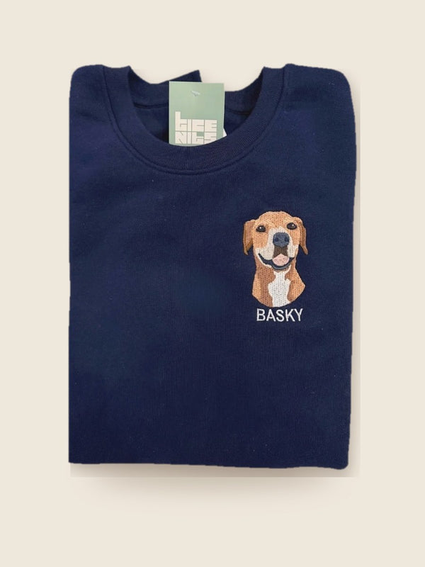Pull bleu marine plié avec un chien brodé et le nom Basky, prêt à partir
