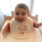 Bavetje - Tice Nits - Baby draagt een wit bavetje met rode tekst. Het slabbetje is gepersonaliseerd met een geborduurde afbeelding. Dit is het geboortekaartje van baby Mia
